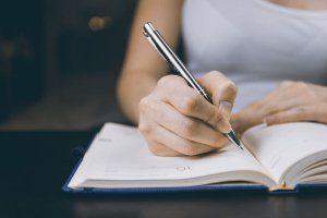 woman writing in a journal with pen